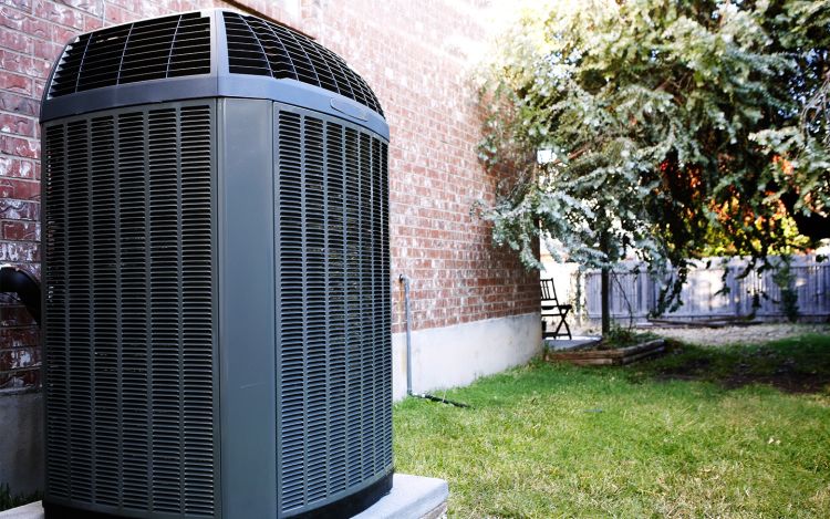 Image of electric heat pump outdoor condenser outside brick house. Modern electric heat pump HVAC systems are remarkably energy efficient and can work in most if not all climates.