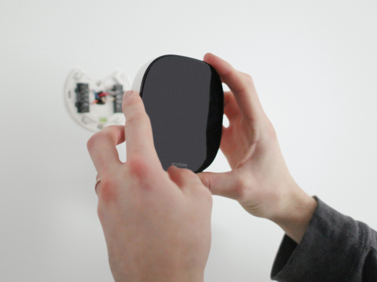 A pair of hands attaches an ecobee thermostat to a wall