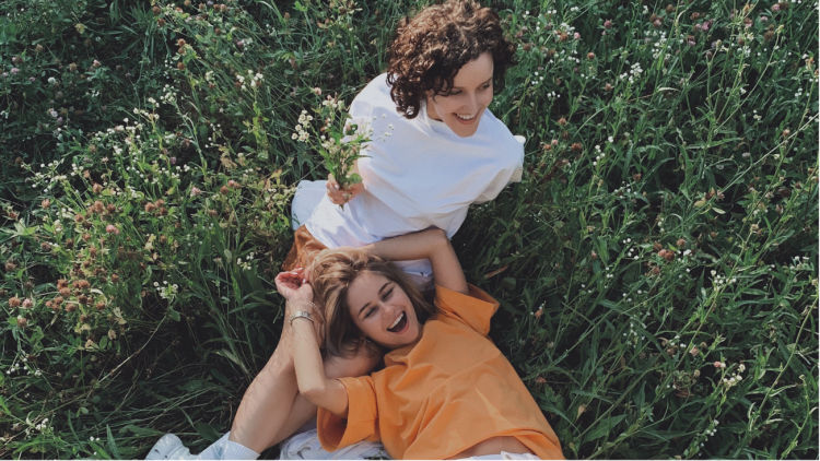 Two women lying down in a field among flowers. 