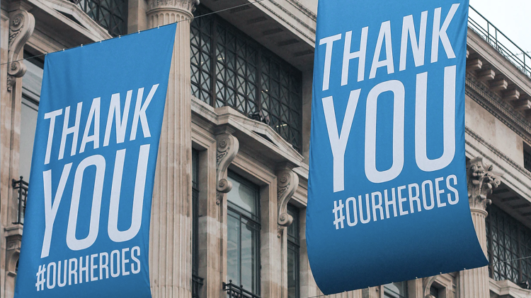 Large blue banners saying "Thank you #ourheroes" hang outdoors.