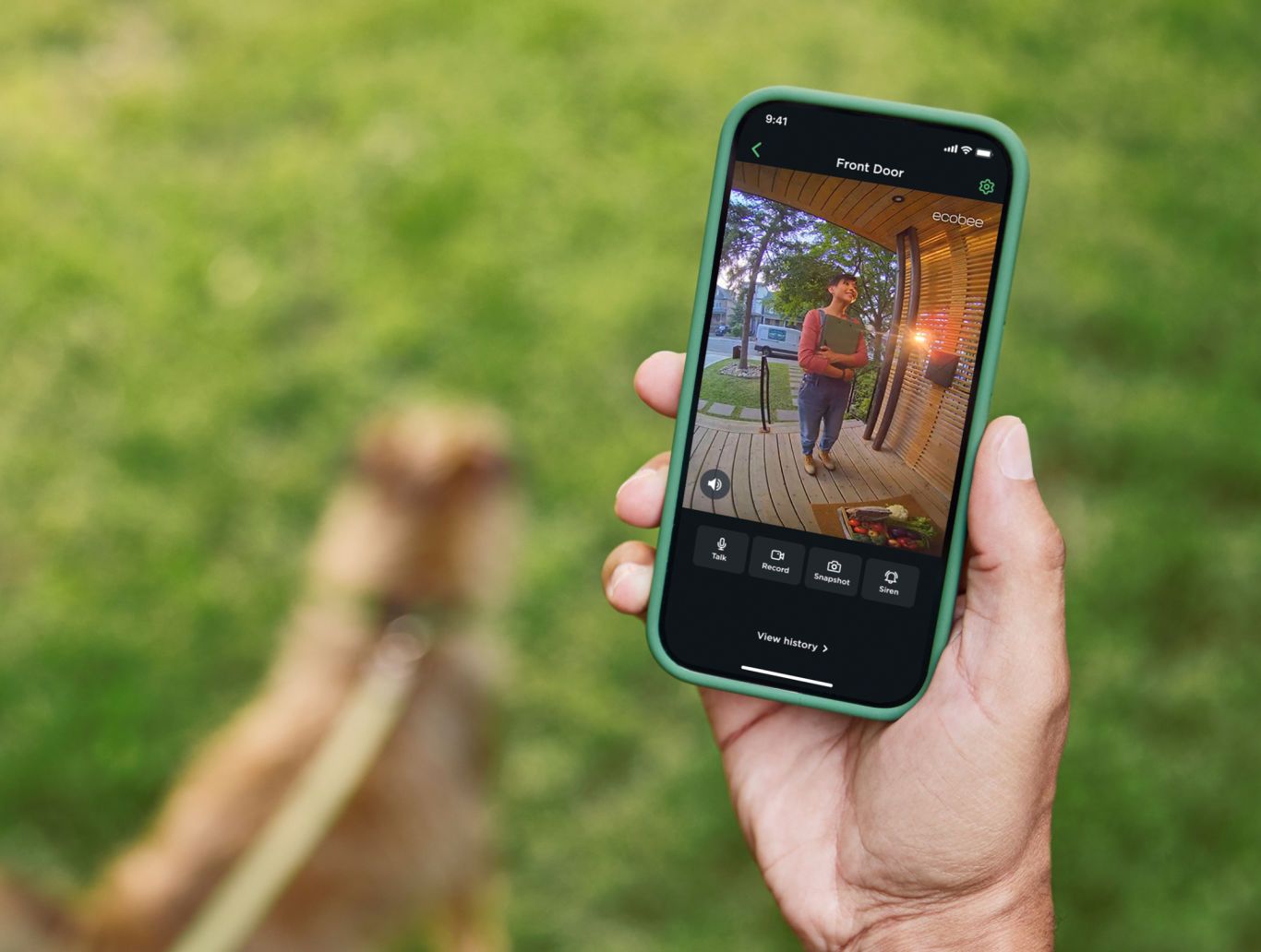 A smart phone with a live view of an individual's front door is held in their hand while they are walking their dog outside