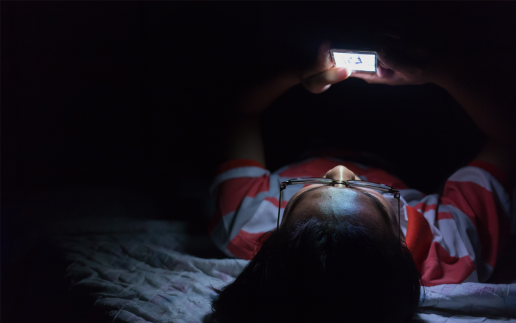 Boy using iPhone in bed at night. Just like an iPhone, pictured laying on table, the data created by ecobee thermostats is encrypted to protect your privacy.