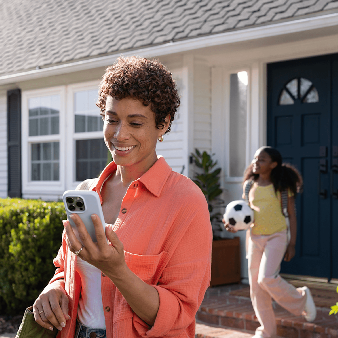 a woman checks her phone while her and her child leave their house