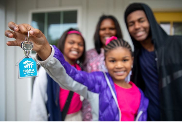 Child in front of family holding up a key with the Habitat for Humanity logo.