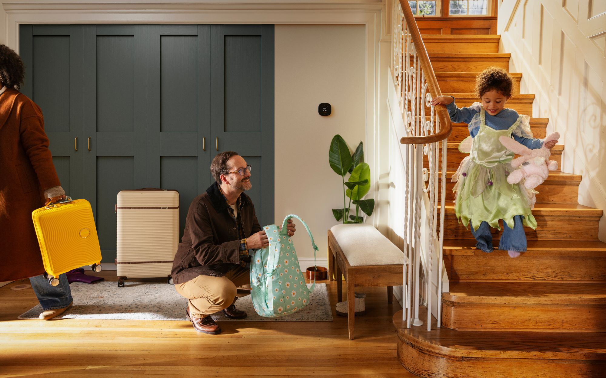 Family preparing to leave home with luggage as a child walks down the stairs near an ecobee smart thermostat displaying 72°F.