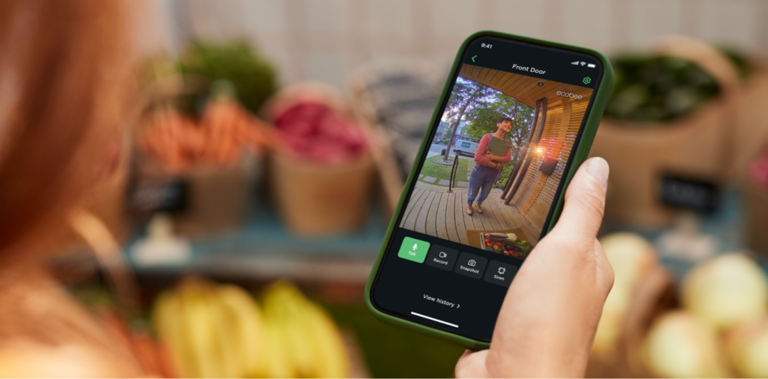 A hand holding a phone with the ecobee app open, using two-way talk to speak to a person at their front door.