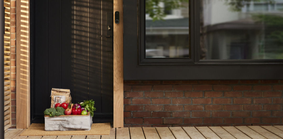 A basket of fruit and vegetables sitting on the ground on a front porch.