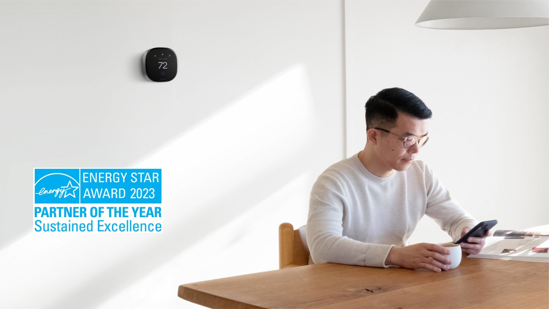 Man sitting at a table with an ecobee thermostat on the wall behind him. ENERGY STAR Partner of the Year logo in the bottom corner.