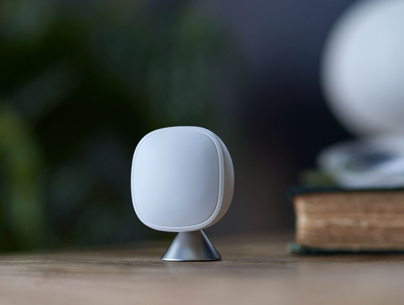 ecobee SmartSensor placed on a wooden desk with plants and a book set in the background