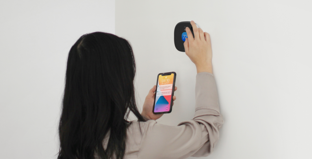 Someone adjusting an ecobee thermostat with their phone in their hand