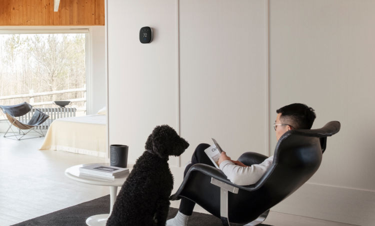 A person sits in a chair reading; an ecobee thermostat is on the wall.