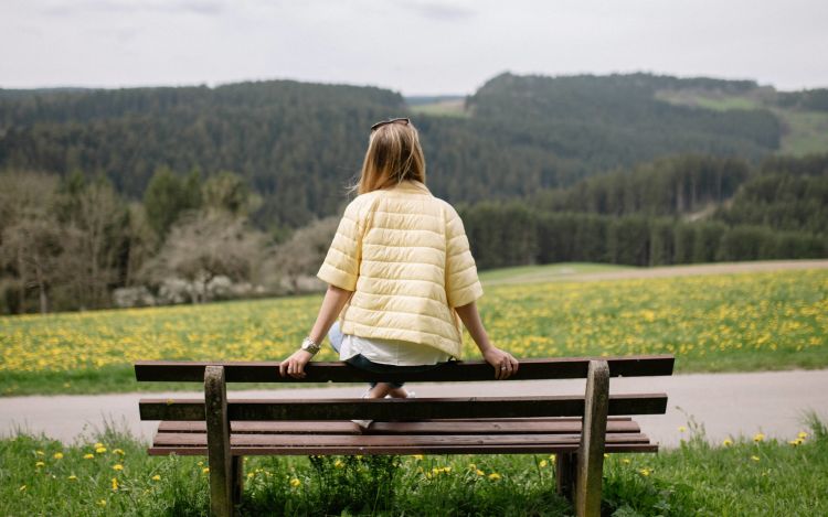 A woman sitting on a bench, overlooking a forest