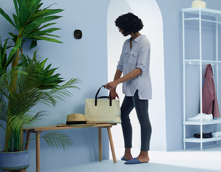A woman gets ready to leave her home while checking her ecobee thermostat.