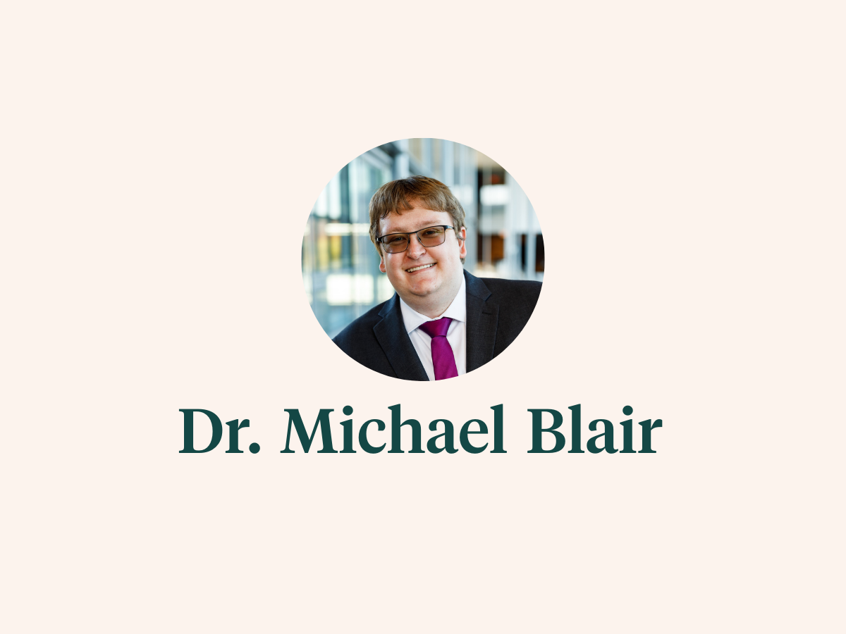 Headshot of Dr. Michael Blair, wearing a suit and tie and dark glasses.