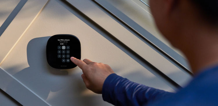 A hand reaches for an ecobee thermostat on a wall.