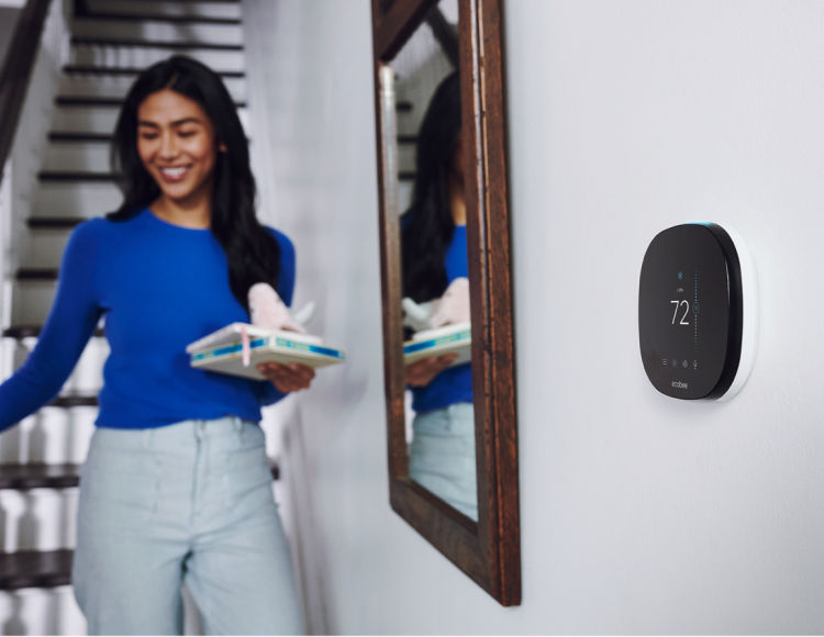 A woman walks by an ecobee thermostat on her wall.