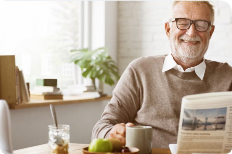 A senior man sits at a table and reads the newspaper