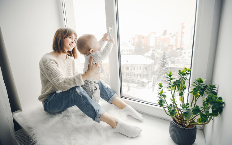 A woman with a baby sit in front of a large, clean window.