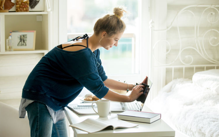 Teenager in blue shirt sets up her bedroom office desk on a sunny morning. 