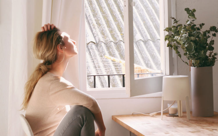 A woman sitting at a desk with one hand on her head, looking out to an open window.