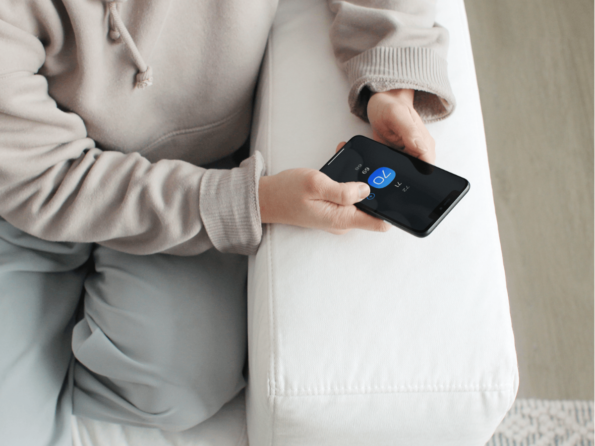Middle-aged person sitting on a couch checking temperature on the ecobee app. 