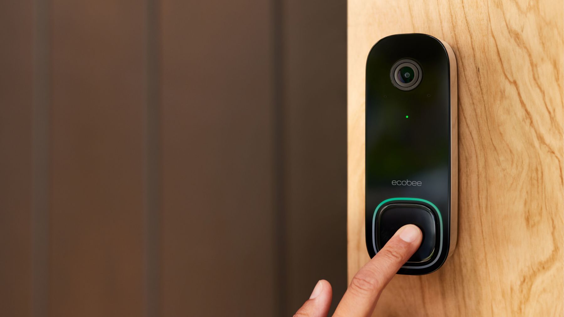 ecobee Smart Doorbell Camera against wooden door frame, with person pressing the button.