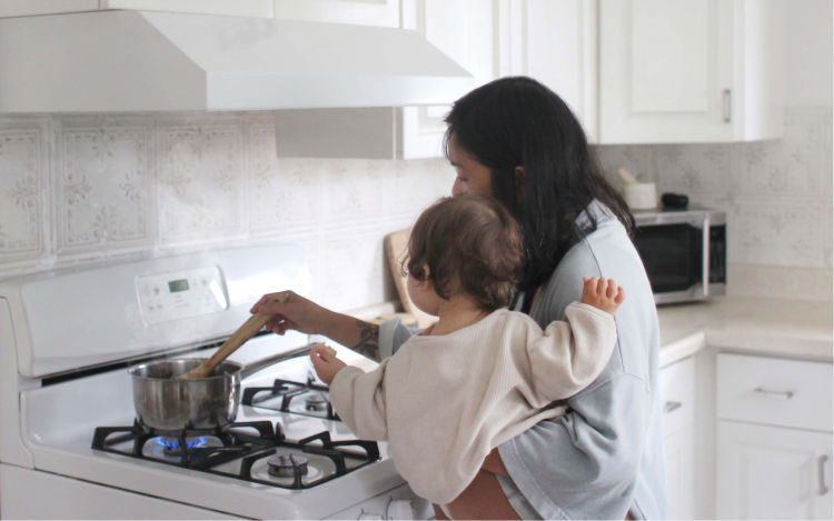 A woman carrying her child and cooking over a gas stove