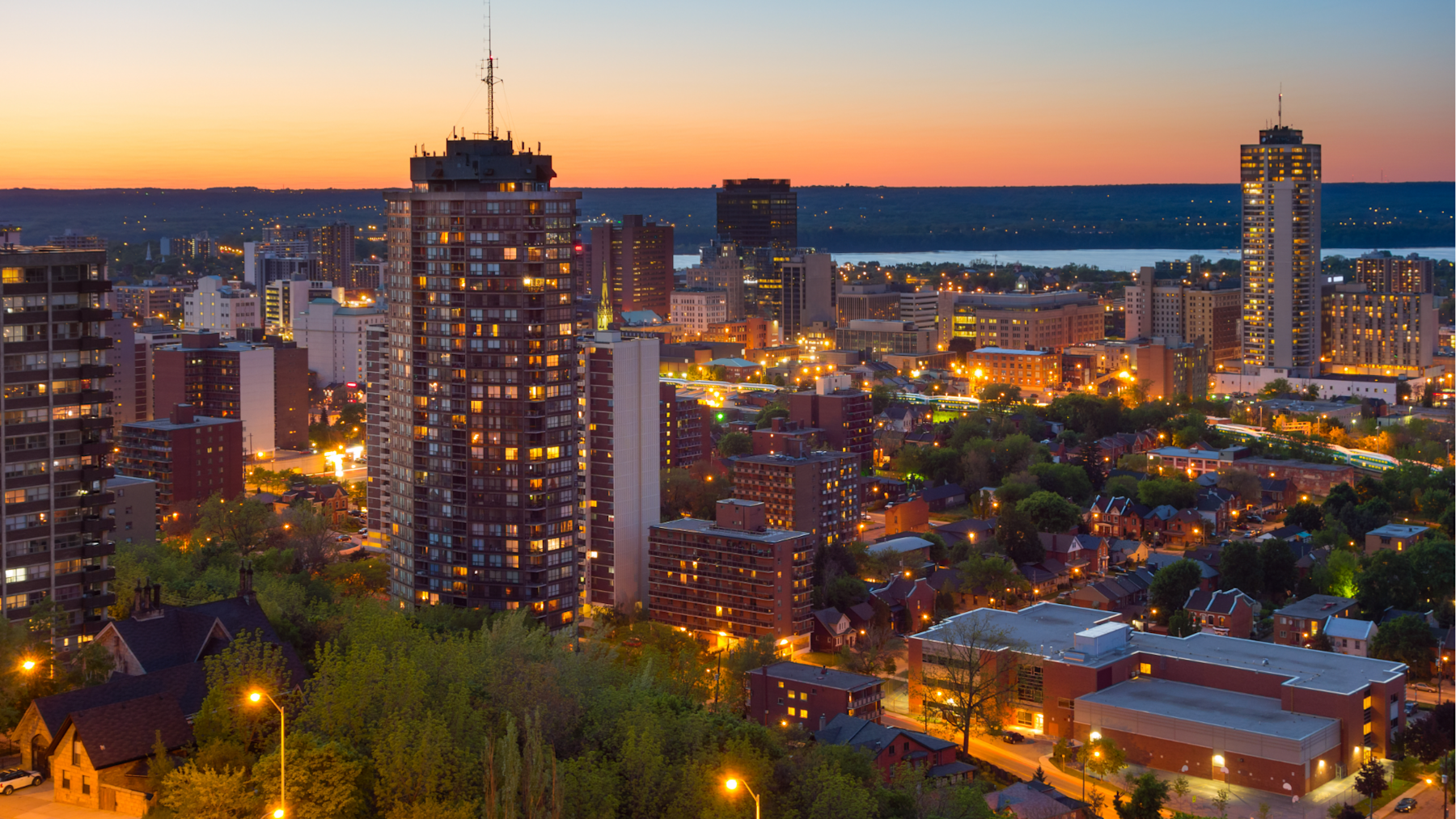 Photo of Hamilton, Ontario with the sunsetting in the background and the foreground is of the city litn up