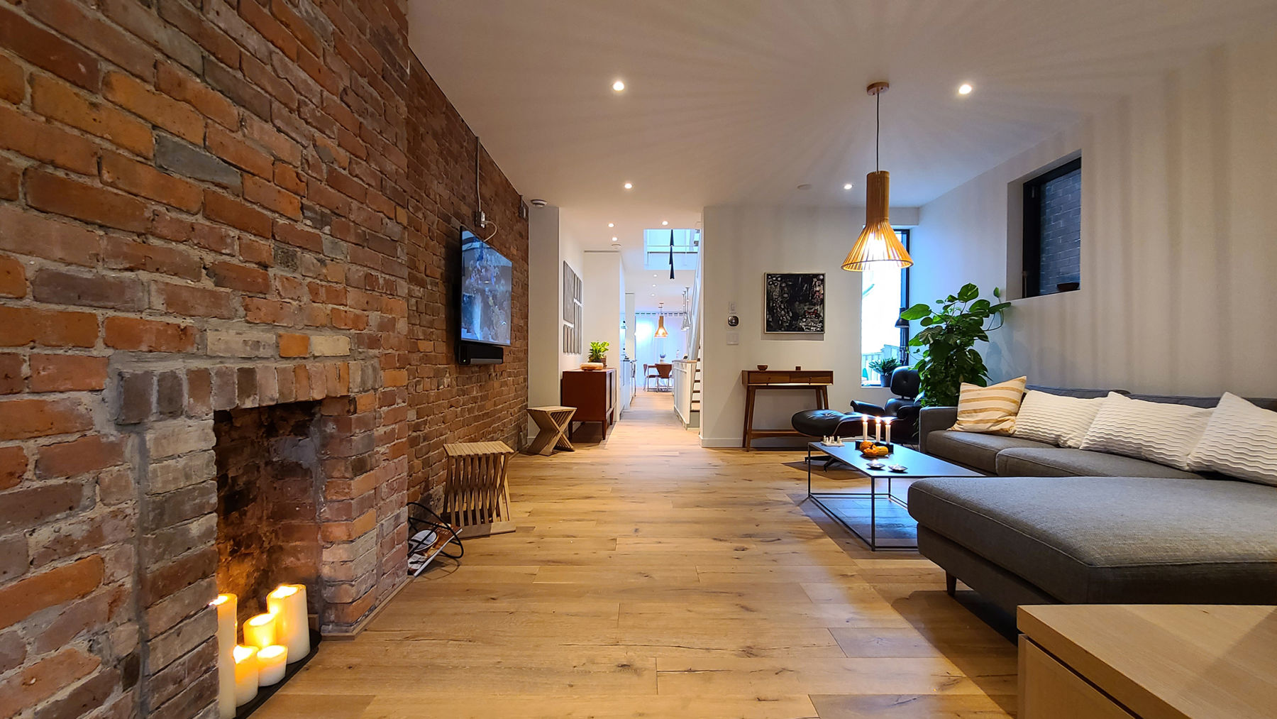 Perfectly conceived Danish modern open-concept living room with l-shaped couch, exposed brick wall, pot lighting, pendant light centerpiece on hardwood floor.  