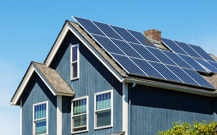 A modern home with royal blue siding, has solar panels on it's roof.