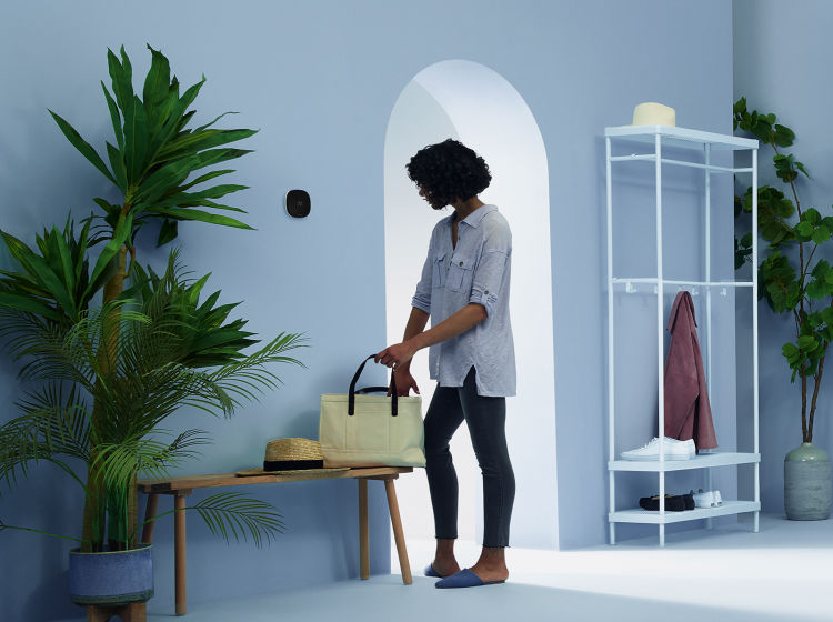 A woman prepares to leave her home with an ecobee thermostat on the wall next to the door.