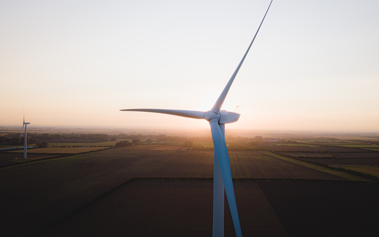 Foreground shot of windmill power generator at twilight set against farm field with other windmills in the distance. Electric heat pumps powered by renewable energy sources like wind and solar will power the homes of tomorrow.