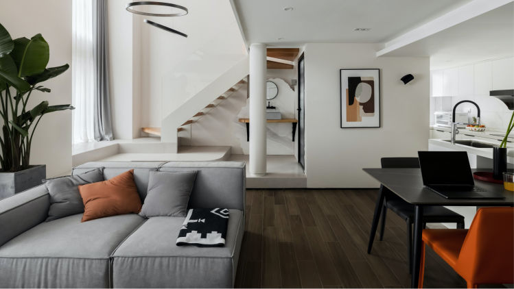 Beautifully designed living room with white walls, grey couch, a plant, and open stairs.