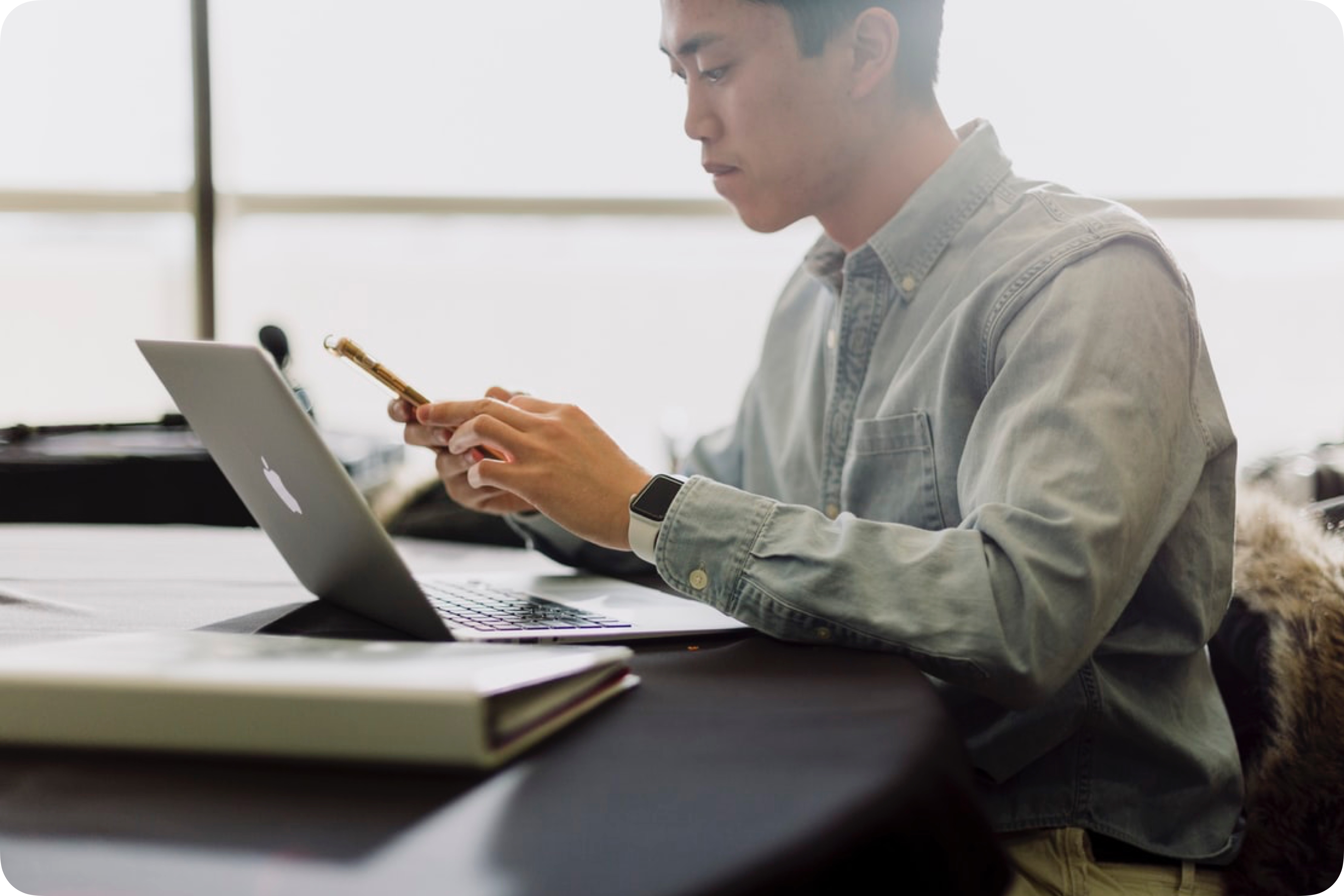 A man sits at a table with a phone and laptop