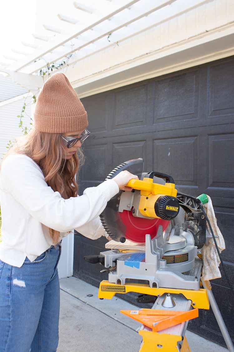 Cass from CASSMAKESHOME cuts a piece of wood with a miter saw.