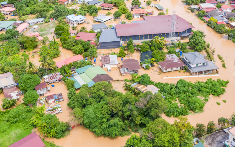 Aerial view of a flooded area in a developing country, with homes submerged under water and scattered trees rising above the floodwaters.