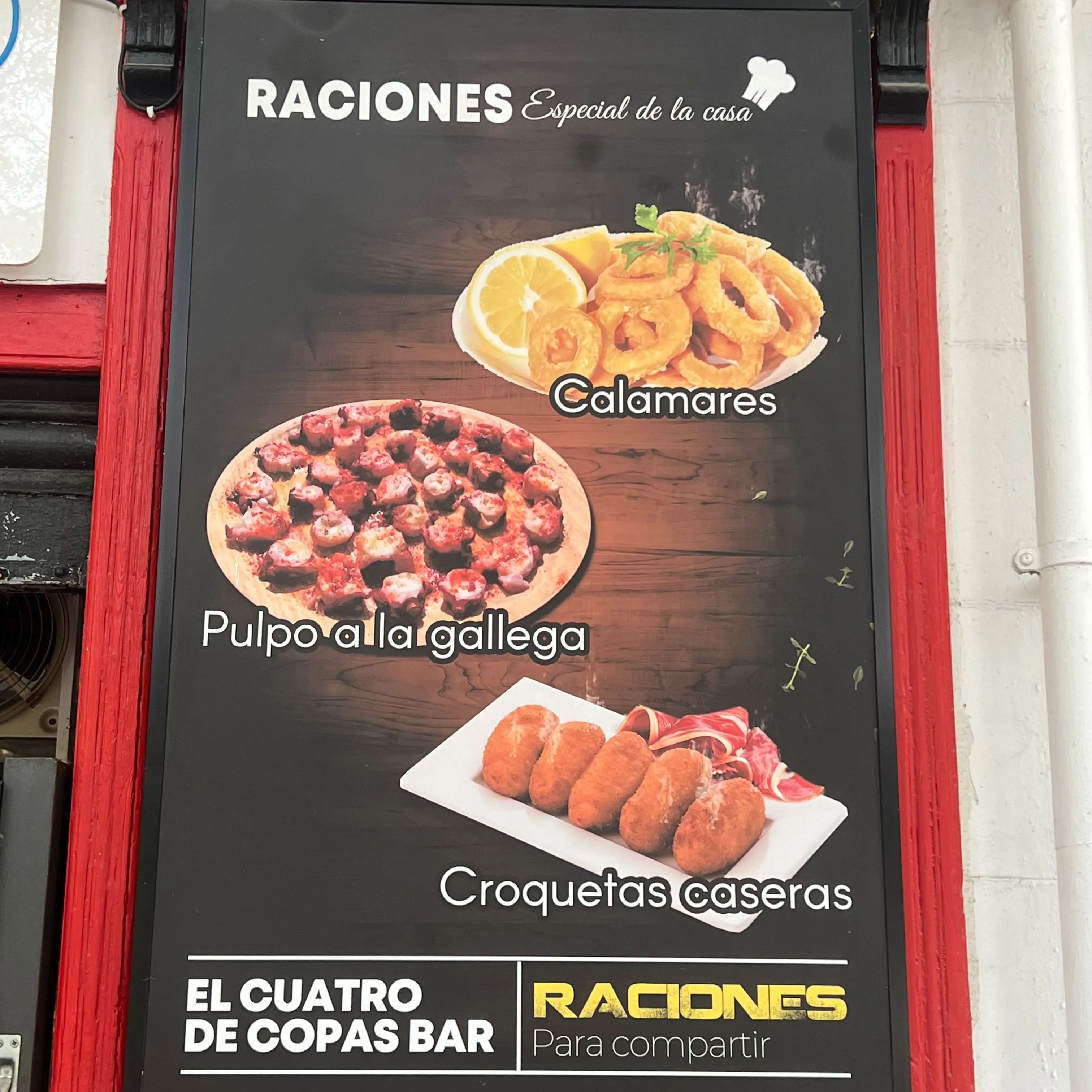 Cartel del bar El Cuatro de Copas que anuncia raciones de la casa con fotos de calamares fritos con limón, pulpo a la gallega y croquetas caseras.