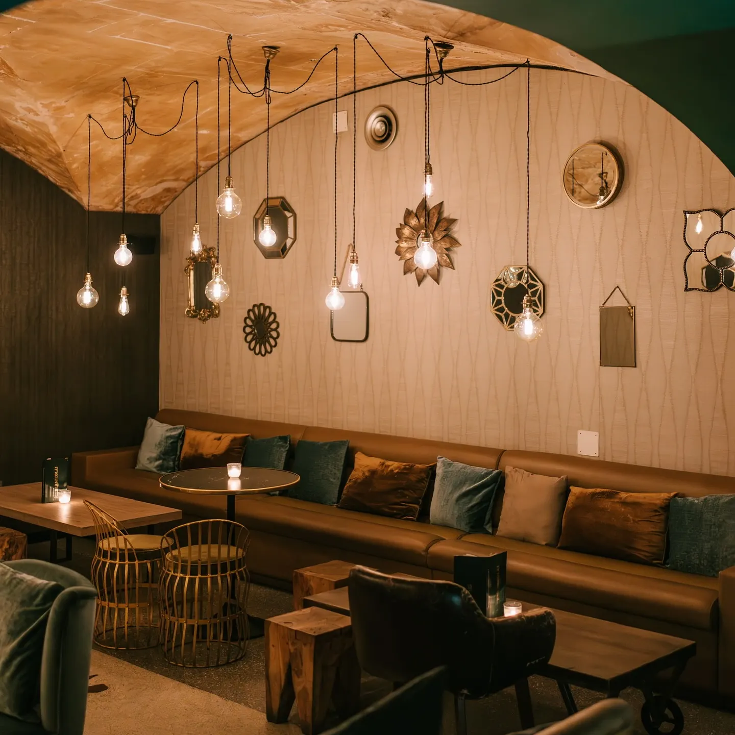 Interior de Bar Nicolás, con iluminación cálida y colgante, sofás de cuero, cojines en tonos cálidos y detalles decorativos elegantes en las paredes.