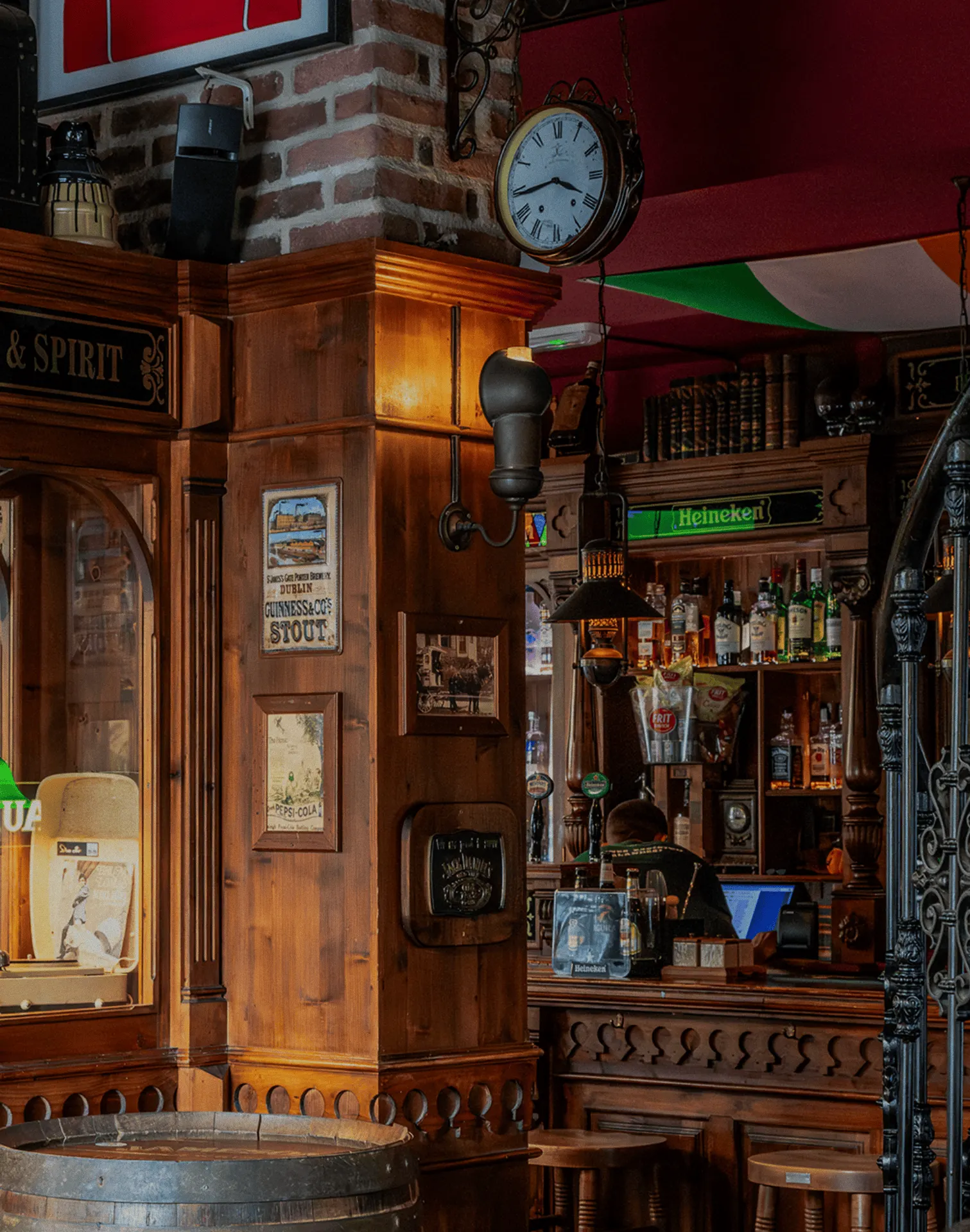 Interior de Mulligan’s con barra de madera tallada, estanterías llenas de botellas, decoración vintage irlandesa y un reloj antiguo colgado sobre ladrillo visto.