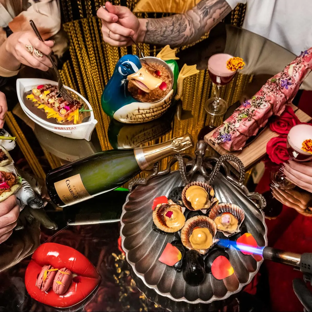 Mesa en Inclán Brutal Bar con platillos creativos, cócteles en vajilla original, botella de cava y decoración excéntrica y vibrante.