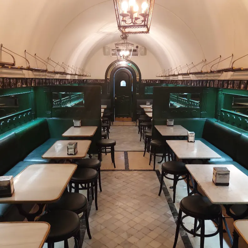 Bóveda blanca, lámparas clásicas y mesas alineadas en el pasillo interior de San Ginés. Tradición y elegancia en cada rincón.