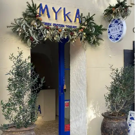 Entrada a Myka Ortega y Gasset con decoración vegetal, puertas azules y dos olivos en maceta que enmarcan el acceso.