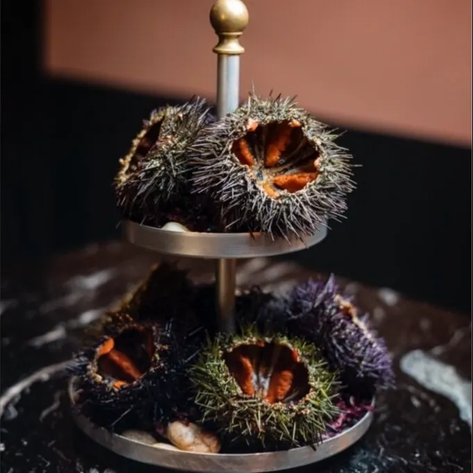 Soporte metálico con erizos de mar abiertos, mostrando su interior naranja, sobre superficie de mármol oscuro.