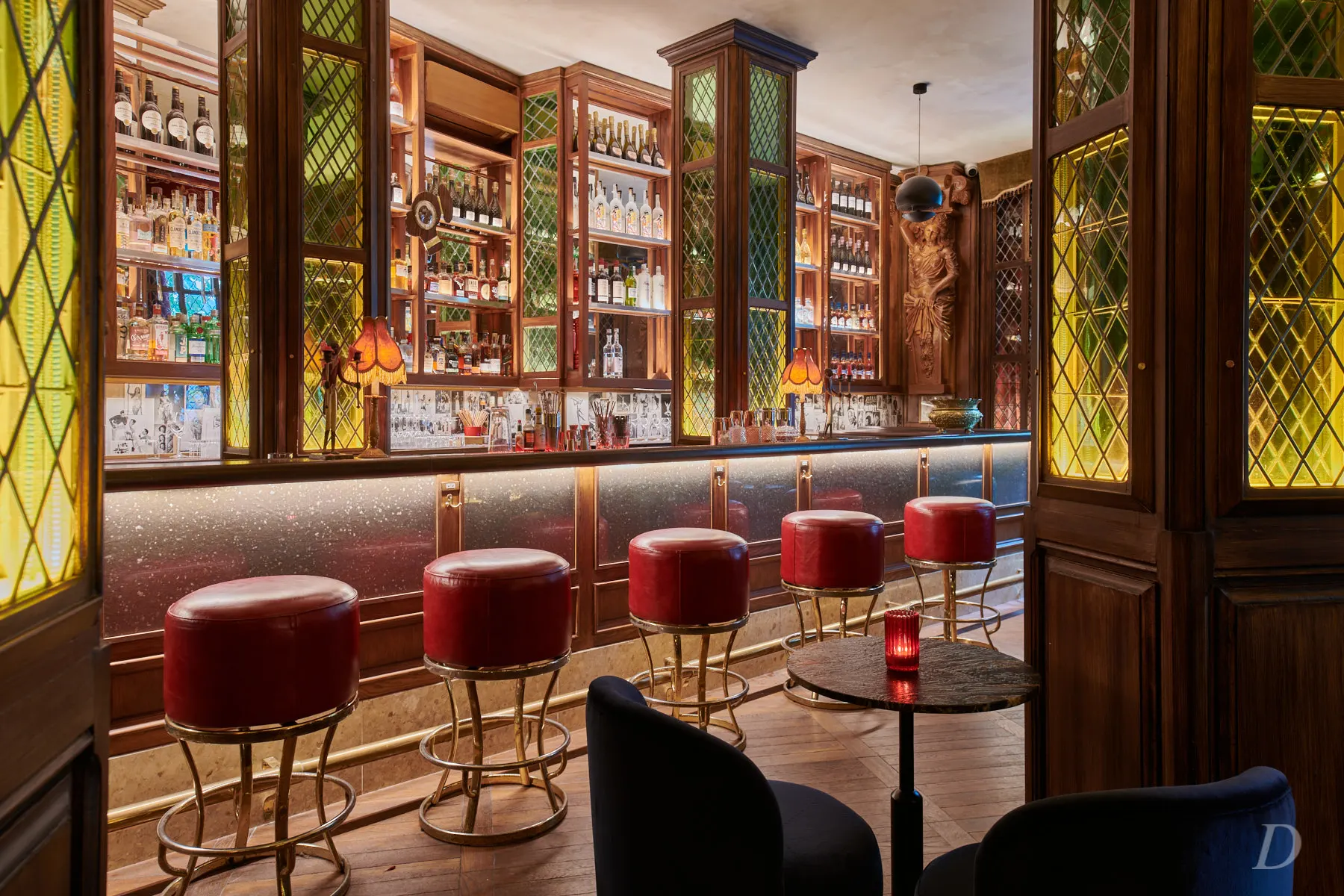 La foto muestra el interior del Nuts indulgence. Hay una larga barra con una superficie blanca, detrás de la cual hay una extensa colección de botellas en estantes que llegan hasta el techo. Los estantes están enmarcados por paneles decorativos verdes.