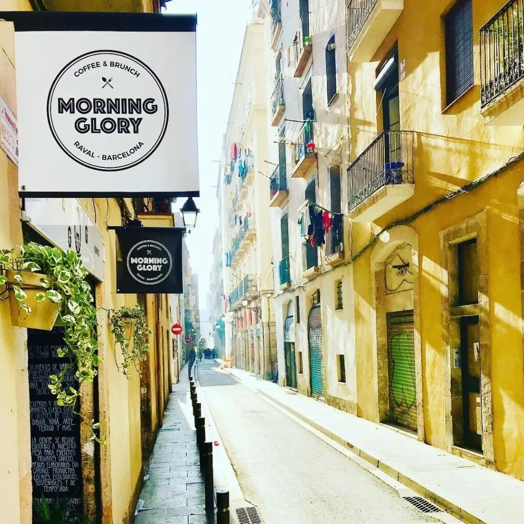 Sándwich gourmet en bagel con salmón, queso crema, tomate y verdes; decorado con puré naranja y hierbas sobre plato negro.