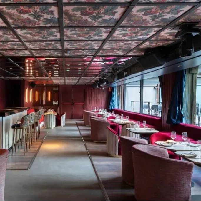 Restaurante moderno con sillas y bancos rojos, mesas redondas, barra central con taburetes y techo decorado con patrón floral.