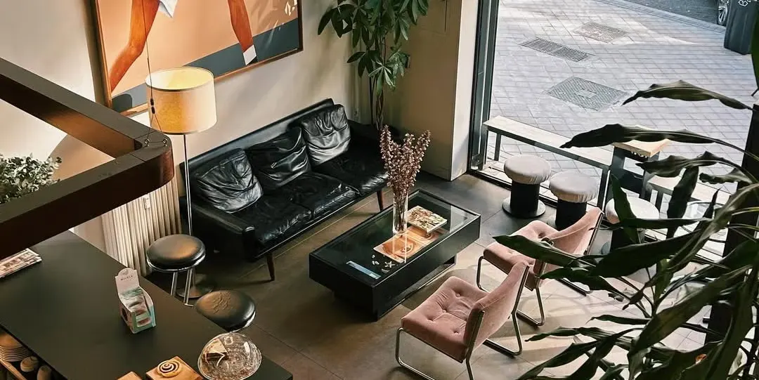 Interior de God Café con mesas alineadas, sillas de madera clara y una barra con luces cálidas que iluminan el espacio moderno