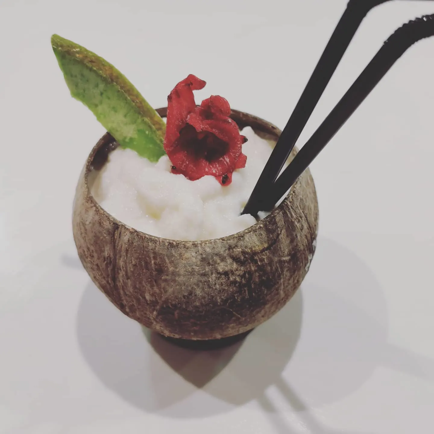 Artadi Beach con un refrescante cóctel tropical servido en un coco, decorado con flor roja y una hoja, ideal para un sorbo exótico.