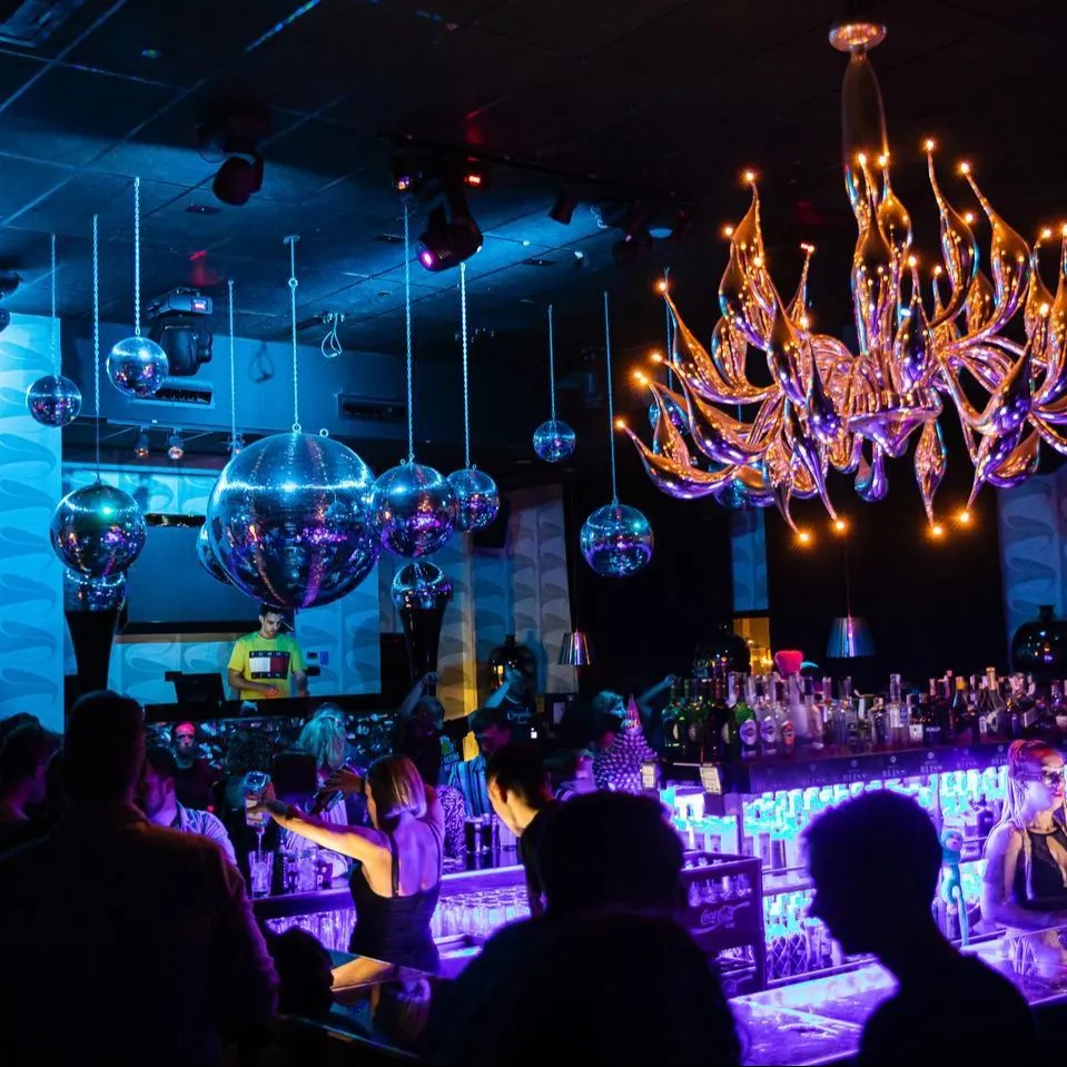 Ambiente retro y moderno, con bolas disco suspendidas y una llamativa lámpara central. La iluminación azul y los detalles metálicos crean un espacio vibrante y elegante.