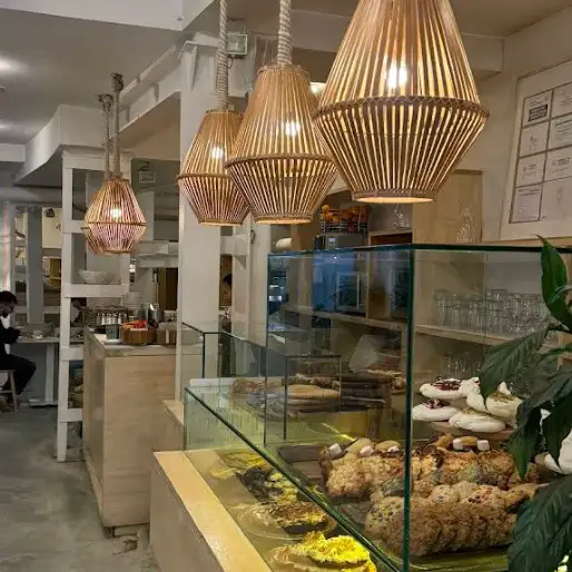 Interior cálido de Mistura Augusto Figueroa con lámparas de mimbre, vitrinas llenas de tartas, cookies y bollería casera.